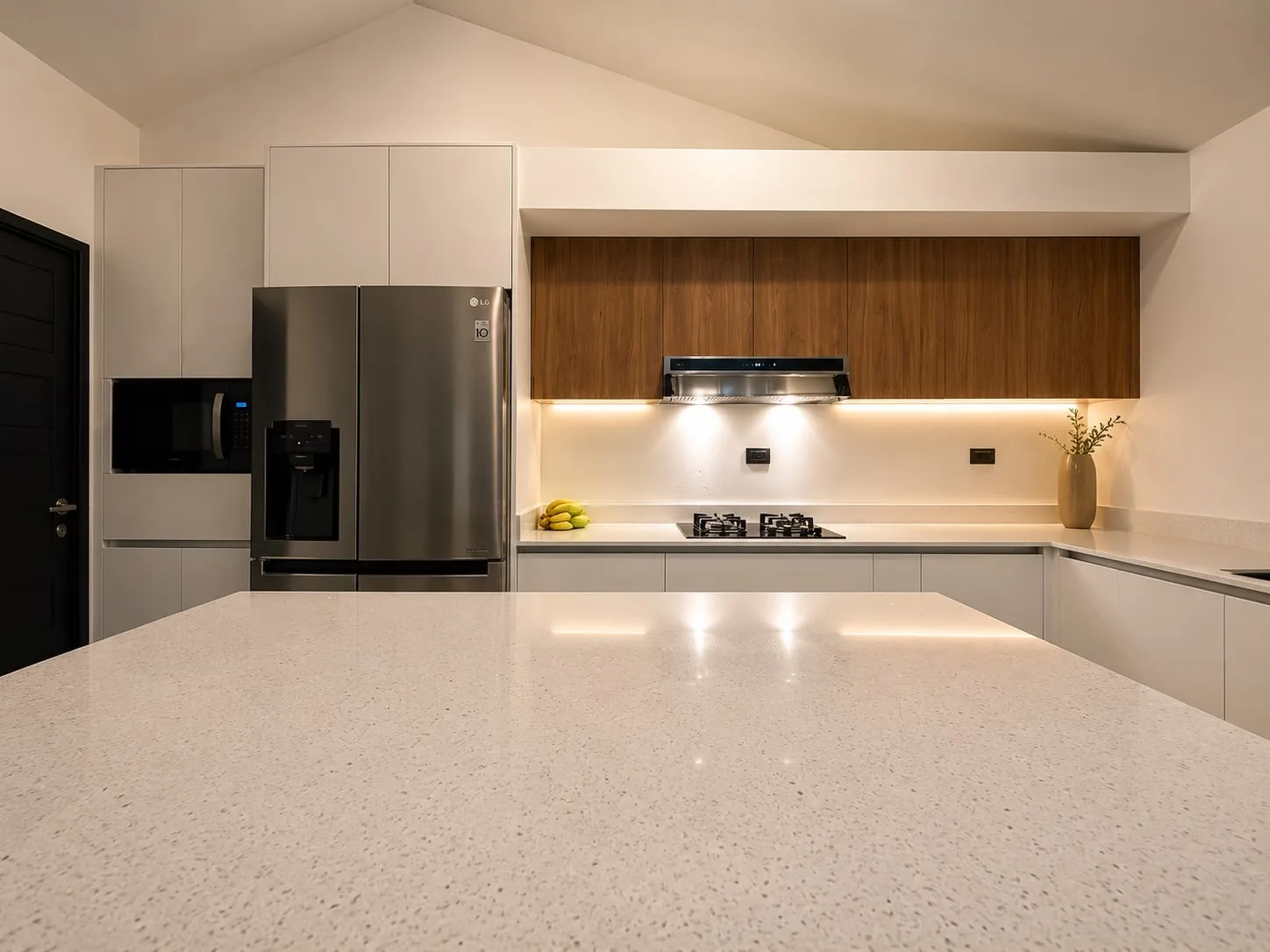 Vista frontal de cocina contemporánea con isla de cuarzo, gabinetes blancos y almacenamiento superior en madera.