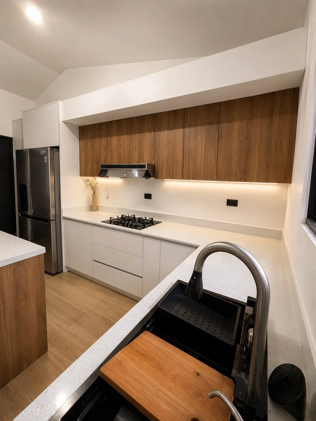 Detalle vertical de cocina instalada con fregadero negro, cubierta clara, iluminación led y gabinetes de madera.