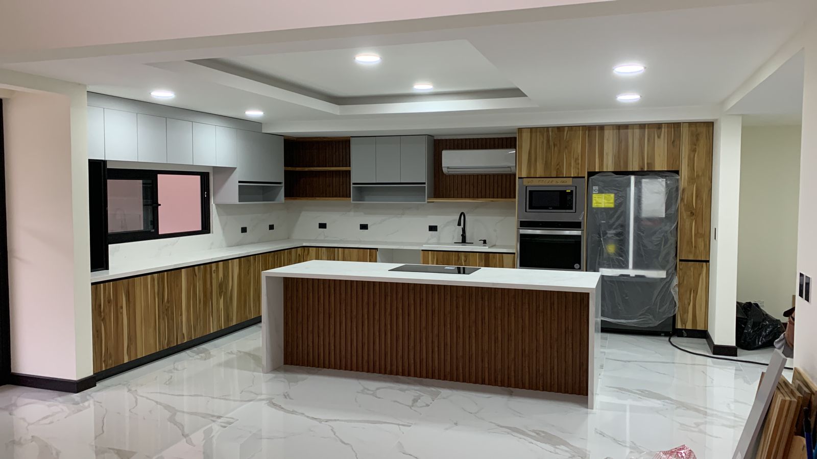 Vista frontal de cocina en U con isla central, frentes en madera cálida y mobiliario superior en tonos claros.