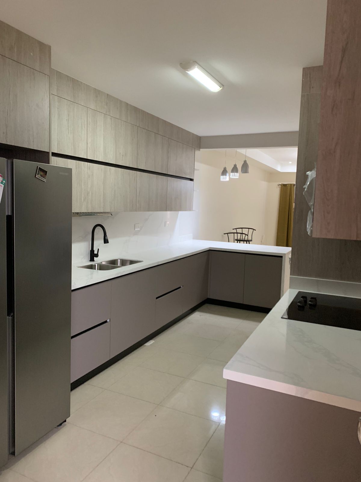 Cocina lineal en tonos taupe con muebles superiores tipo madera clara y sobre blanco continuo.