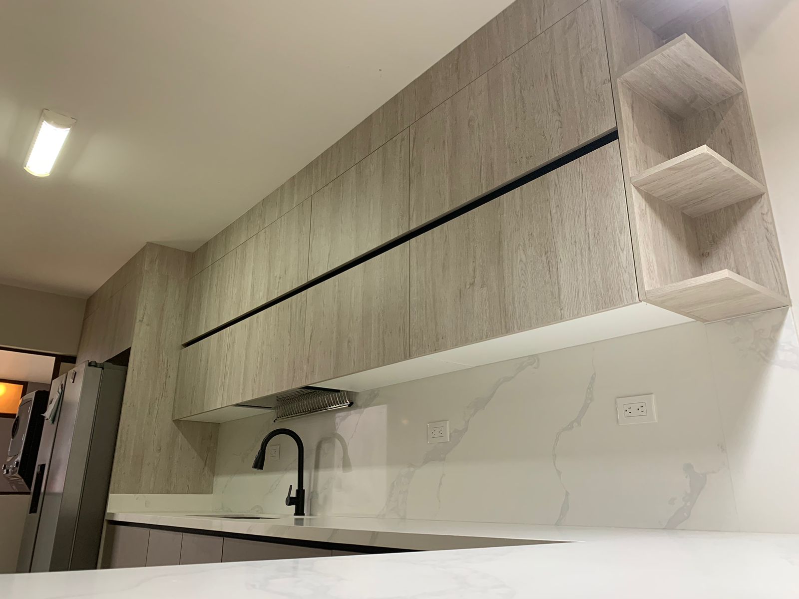 Detalle lateral de cocina minimalista con mobiliario alto en madera clara y grifería negra mate.