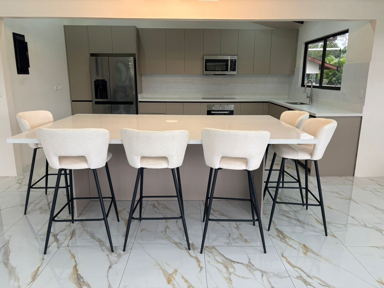 Vista frontal de cocina abierta con barra blanca y taburetes tapizados frente al mobiliario lineal.