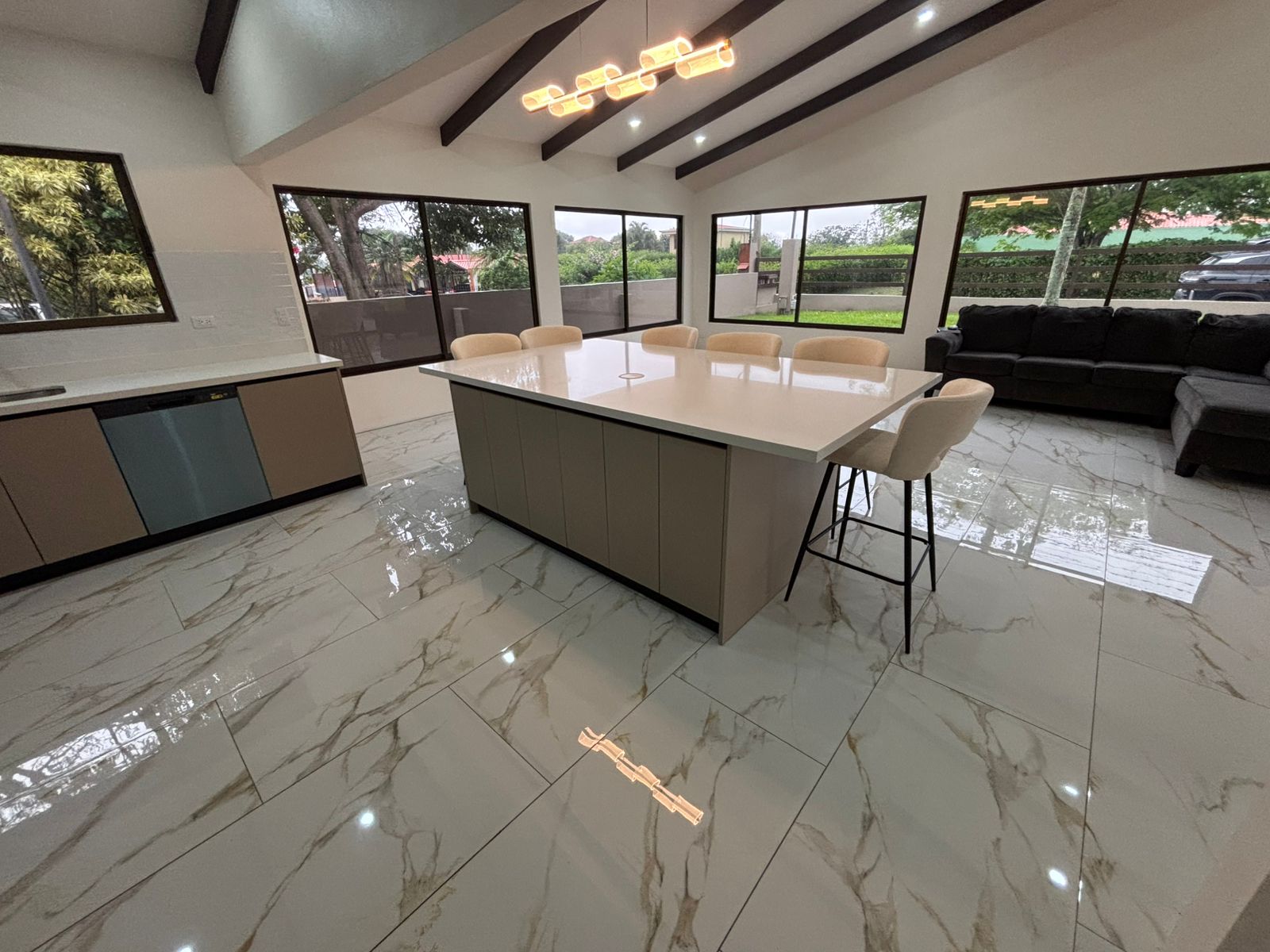 Vista general de cocina y área social con isla central, grandes ventanales y piso tipo mármol.