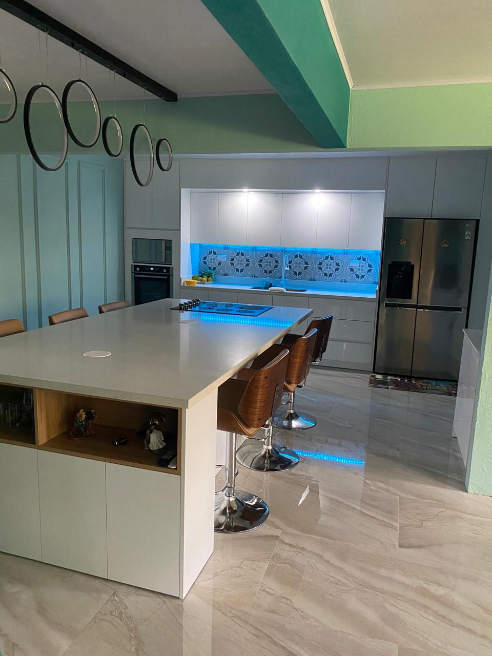 Vista diagonal de cocina integrada con barra, taburetes y detalles de iluminación led en la zona de trabajo.