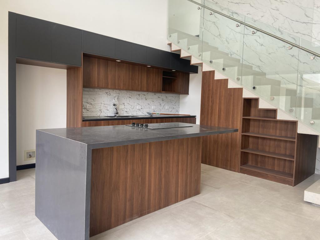 Cocina bajo escalera con isla en acabado cemento y madera oscura, de estilo contemporáneo urbano.